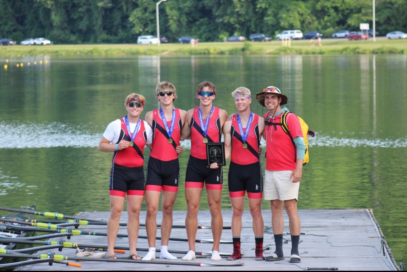 Five UGA Rowing members wearing red shirts pose in front of the water.